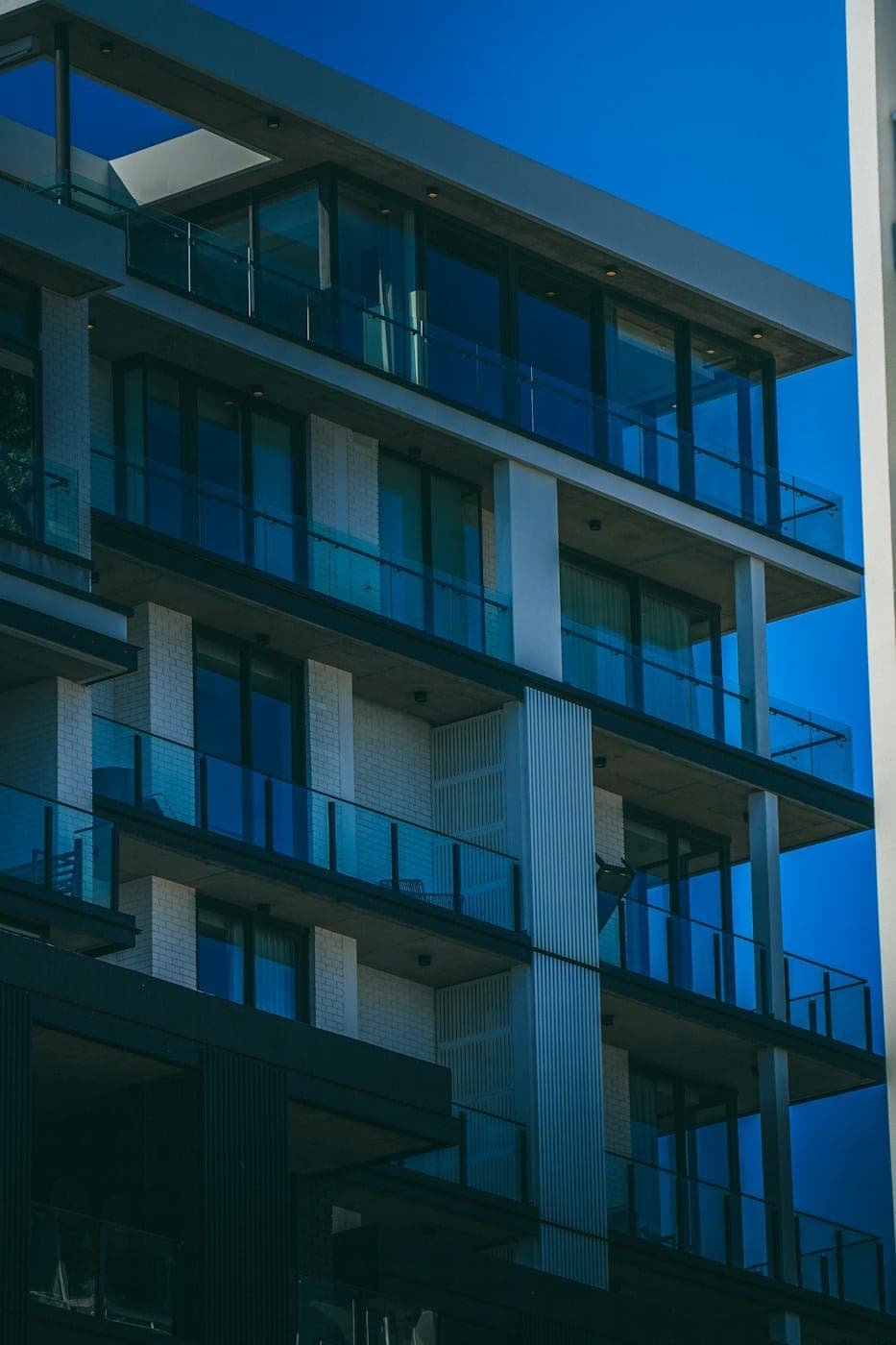 Modern apartment building with glass balconies on every floor against a deep blue sky